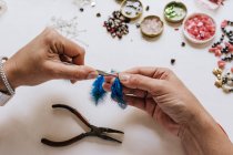 High angle of crop designer with pincers making decorative bijouterie sitting at table with different crystals and sequins — Stock Photo