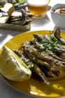 From above of delicious fried anchovies served on plates with lemon and placed on white table with glass of beer - foto de stock