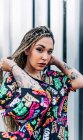 Junge coole Frau in trendiger Kleidung mit Afro-Zöpfen blickt gegen gerippte Wand in der Stadt in die Kamera — Stockfoto