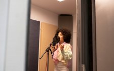 Black female singer performing song against microphone with pop filter while standing and closed eyes in sound studio — Stock Photo