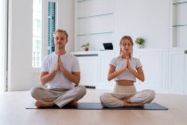 Мирная пара сидит в позе лотоса с молитвенными руками, практикуя йогу вместе и медитируя с закрытыми глазами — стоковое фото