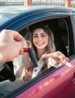 Ernte unkenntlich Person übergeben Fahrzeugschlüssel an zufriedene junge Fahrerin Blick auf Kamera aus modernen Automobil in der Stadt — Stockfoto
