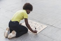 High angle side view of African American female activist writing Black Lives Matter and making placard for protest against racism in city — Fotografia de Stock
