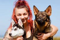 Content female athlete with piercing embracing Siberian Husky and German Shepherd while looking at camera in sunlight — Stock Photo