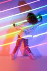 Full body back view of stylish confident African American female dancer with curly hair and sunglasses standing in neon lights in dancing studio — Stock Photo