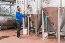 Vista laterale dell'imprenditore maschio che parla sul cellulare contro i vasi in acciaio inossidabile sul pavimento bagnato nella fabbrica di birra — Foto stock