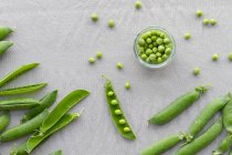 From above of glass small bowl with crispy green peas near pile of crunchy pea pods on table at home — Stock Photo
