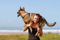 Татуйована жінка-спортсменка з милою чистою собакою на плечах дивиться на камеру в сонячний день — стокове фото