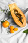 Half of pawpaw with seeds between tangerines and cumquats with leaves on white crumpled cloth — Photo de stock