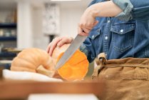 Coltivare femmina con coltello affilato tagliare zucca cruda sul tagliere durante la cottura in cucina a casa — Foto stock