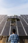 Volver ver anónimo técnico profesional con camisa a cuadros comprobación de paneles fotovoltaicos en la central solar en tiempo claro y soleado - foto de stock