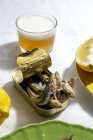 From above of delicious fried anchovies served on can with lemon and placed on white table with glass of beer — Fotografia de Stock