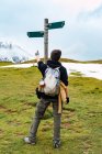 Back view of female backpacker pointing on arrow showing footpath direction standing against pole in Peak of Europe — Stock Photo