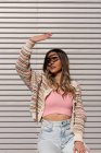 Mujer joven en ropa elegante con la mano levantando los vasos sentados en la valla y con los ojos medio cerrados en la ciudad - foto de stock