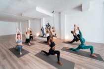 Vue latérale à angle élevé du groupe de diverses personnes en tenue de sport debout à Anjaneyasana et étirant les corps pendant les cours de yoga en studio — Photo de stock