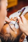 High angle of crop unrecognizable cosmetologist with tweezers applying fake eyelashes for extension on eye of ethnic client in salon — Foto stock