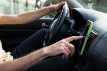 Side view of cropped unrecognizable male driver checking direction on GPS navigator on smartphone while traveling through countryside in summer day — Stock Photo