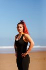 Самозабезпечена жінка-спортсменка з руками на стегнах дивиться на піщаний океан на сонячному світлі — стокове фото