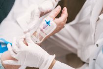 High angle of crop anonymous medic in disposable gloves putting intravenous catheter on arm of patient in hospital — Stock Photo
