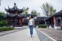 Азиатская женщина, гуляющая в китайском саду с традиционной архитектурой на заднем плане — стоковое фото