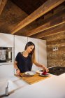 Content female with knife cutting ripe strawberry while preparing healthy food in bowl at home — Foto stock
