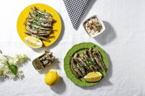 From above of fried and canned anchovies served on table with fresh lemons in restaurant in sunlight - foto de stock