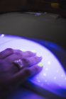 Crop anonymous female putting hands into UV nail lamp dryer for gel polish after manicure - foto de stock