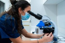 Vista lateral del veterinario femenino en uniforme azul mirando a través del microscopio mientras trabaja en laboratorio - foto de stock