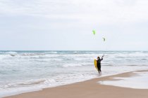 Sportlerin im Neoprenanzug mit Steuerstange blickt nach Kiteboarding-Übung am Sandstrand gegen schäumenden Ozean weg — Stockfoto