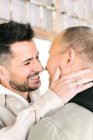 Side view of happy young multiracial gay couple hugging and looking at each other on street on sunny day — Stock Photo