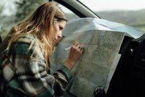 Vista lateral da turista focada tomando notas no mapa da rota enquanto está sentada no automóvel — Fotografia de Stock