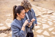From above adult mother in casual wear pointing at wristwatch on hand of boy while interacting on rough walkway — Foto stock