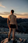 Anonyme männliche Wanderer in schwarzen Unterhosen stehen auf felsigen Berggipfeln und bewundern spektakuläre Hochlandkulissen bei Sonnenuntergang — Stockfoto