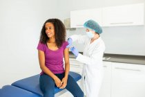 Ärztin in Schutzuniform, Latexhandschuhen und Gesichtsmaske impft glückliche afroamerikanische Patientin in Klinik während des Coronavirus-Ausbruchs — Stockfoto