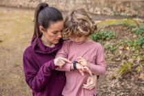 From above adult mother in casual wear pointing at wristwatch on hand of boy while interacting on rough walkway — Photo de stock