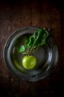 De arriba manzana verde madura con follaje en plato sobre fondo de mesa de madera - foto de stock