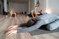 Masculino flexible irreconocible practicando yoga en Kapotasana mientras estira las piernas durante la clase de yoga en estudio - foto de stock
