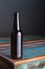 Dark glass bottle of alcoholic drink on painted square shaped wooden table at home — Stock Photo