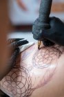 Tatuagem feminina com tatuagem de desenho de máquina no corpo do cliente irreconhecível no salão — Fotografia de Stock