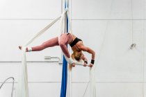 Sportiva flessibile a figura intera in activewear che pratica esercizi aerei su sete in un moderno club sportivo attrezzato — Foto stock