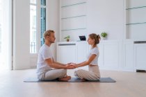 Seitenansicht eines friedlichen Paares, das in Lotus-Pose sitzt und Händchen hält, während es gemeinsam Yoga praktiziert und mit geschlossenen Augen meditiert — Stockfoto