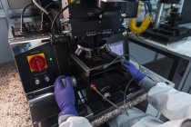 Zugeschnittene, nicht wiederzuerkennende Expertin in Labormantel-Handschuhen untersucht Proben durch leistungsstarke Mikroskoplinsen, während sie in modern ausgestatteten Labors arbeitet — Stockfoto