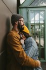 Seitenansicht des jungen stilvollen Paares, das sich sanft umarmt, während es auf der Holzterrasse in der Nähe des Hauses steht — Stockfoto