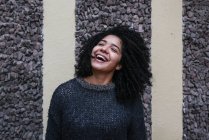 Зміст етнічної жінки з африканською зачіскою, що кидає волосся, стоячи на вулиці і посміхаючись — стокове фото