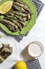 From above of delicious fried anchovies served on plates with lemon and placed on white table with glass of beer — Fotografia de Stock