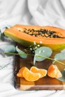 Half of pawpaw with seeds between tangerines and cumquats with leaves on white crumpled cloth - foto de stock