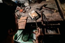 From above anonymous craftsman at workbench using hot torch and melting small pieces of metal — Stock Photo