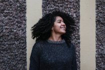 Zufriedene ethnische Frau mit Afrofrisur, die Haare wirft, während sie auf der Straße steht und lächelt — Stockfoto