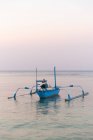 Petit bateau de pêche amarré sur de l'eau de mer turquoise sous un ciel bleu sans nuages au crépuscule paisible — Photo de stock