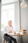 Жінка-астролог робить нотатки в блокноті за столом з чашкою кави вдома на сонячному світлі — стокове фото
